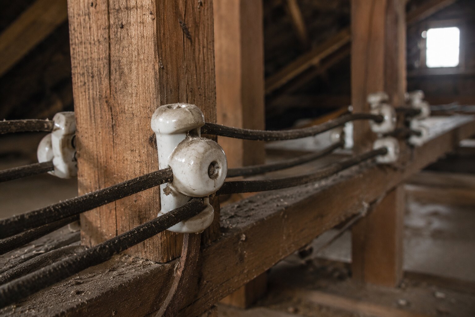 Close-up of vintage knob-and-tube electrical wiring with ceramic insulators in a home attic.